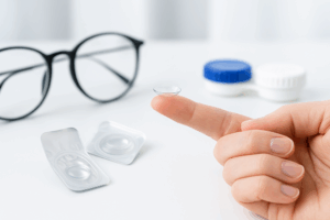 Lentilles réutilisables ou lentilles jetables posées sur un doigt avec étui et lunettes en arrière-plan